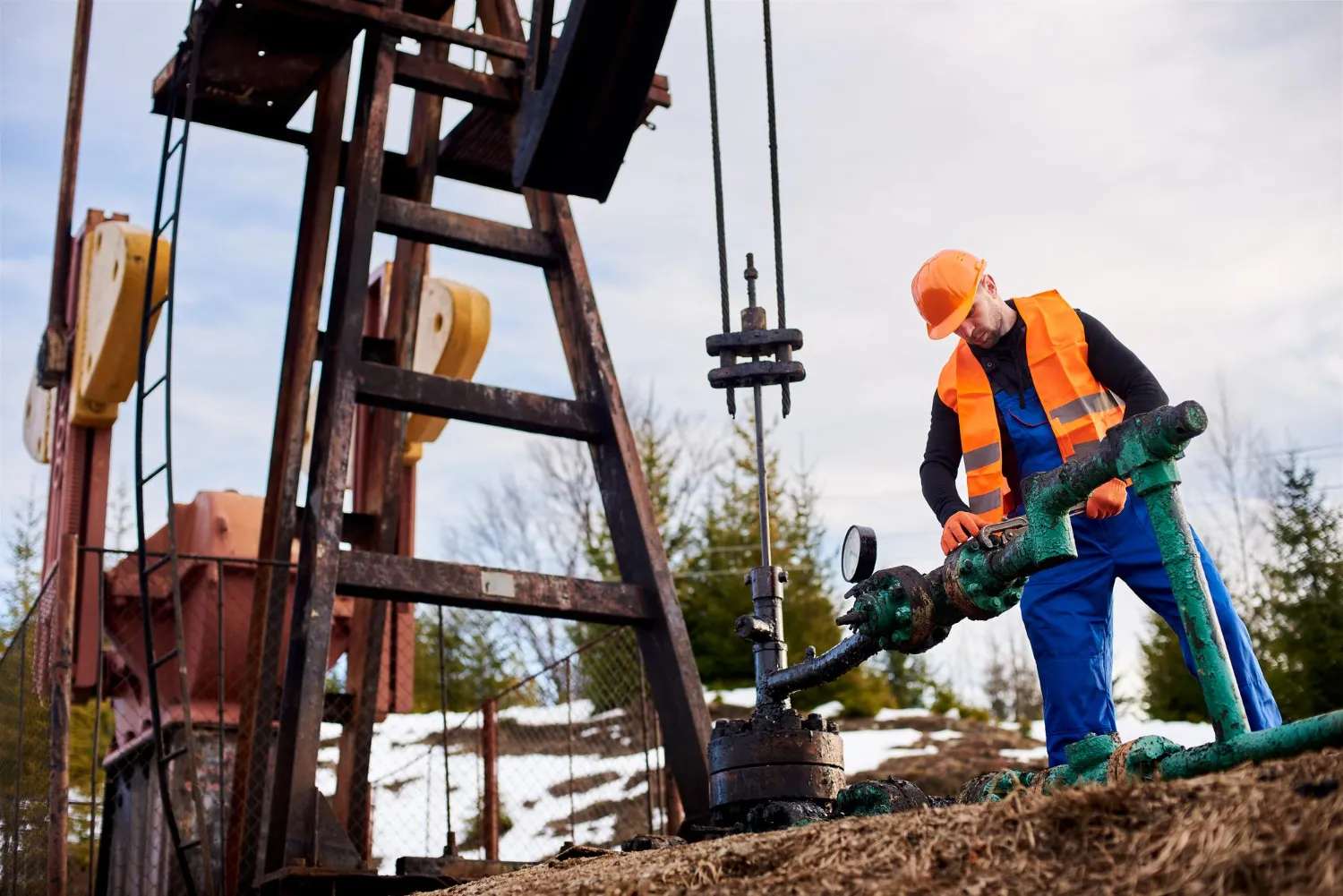 2146 Oil worker in orange uniform and helmet working with a pipe wrench near an oil pump jack
